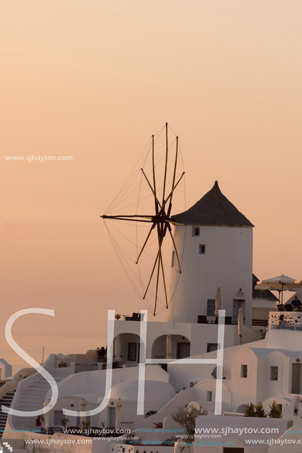 Sunset over white windmills in  town of Oia and panorama to Santorini island, Thira, Cyclades, Greece