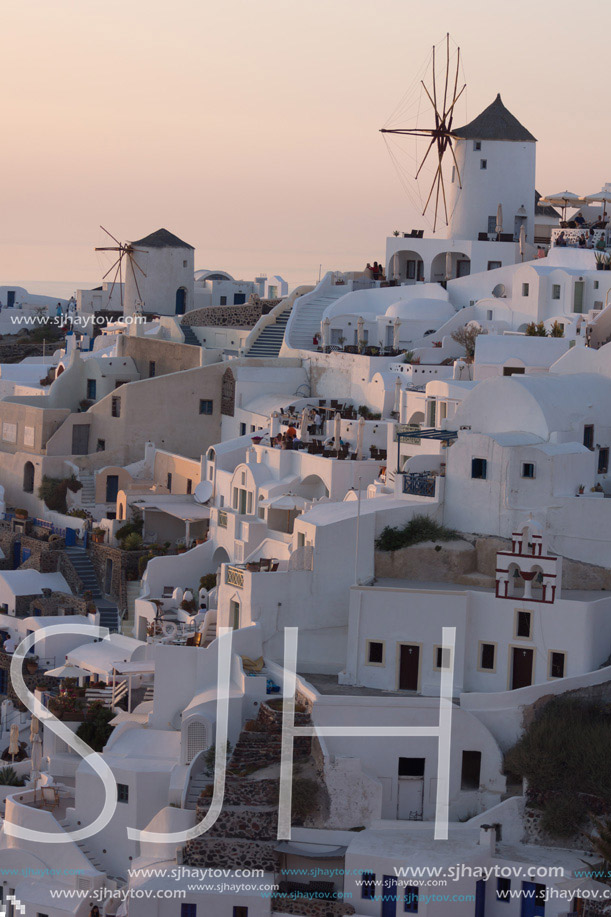 Sunset over white windmills in  town of Oia and panorama to Santorini island, Thira, Cyclades, Greece